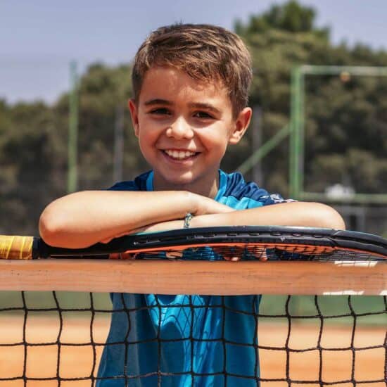 Kid playing tennis outdoors at Bradford International Virtual School tennis court, smiling, happy, youth sports education, virtual school sports activities, school sports programs.